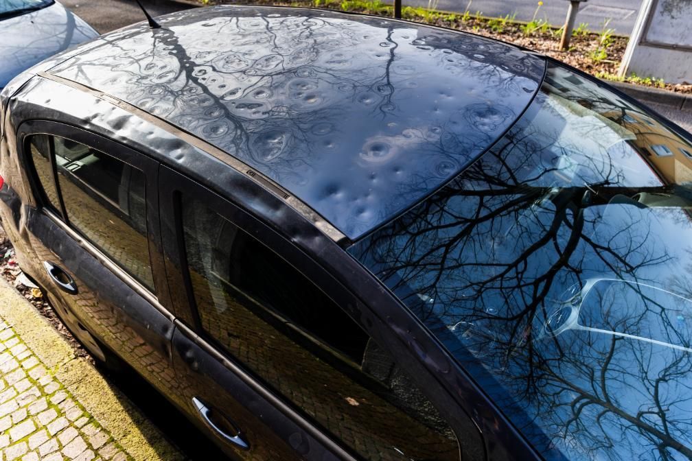 A Black Car with A Hail Damaged Roof Is Parked on The Side of The Road — Dent Repair Specialist in Maroochydore, QLD