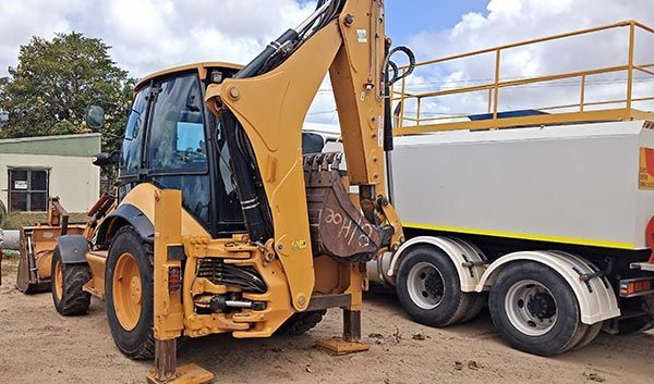 A backhoe is parked next to a white truck.
