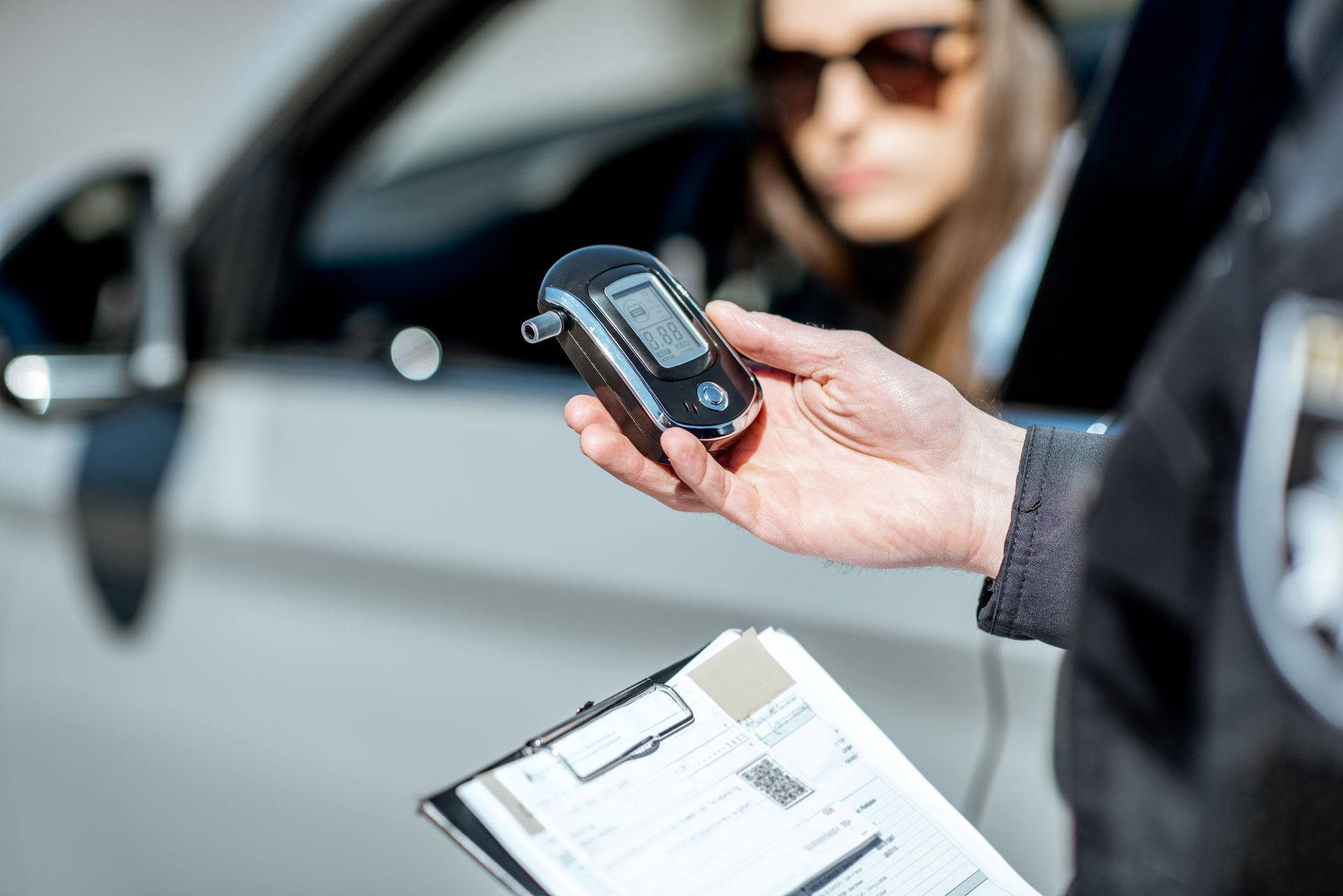 A man is holding a breathalyzer in front of a woman in a car.