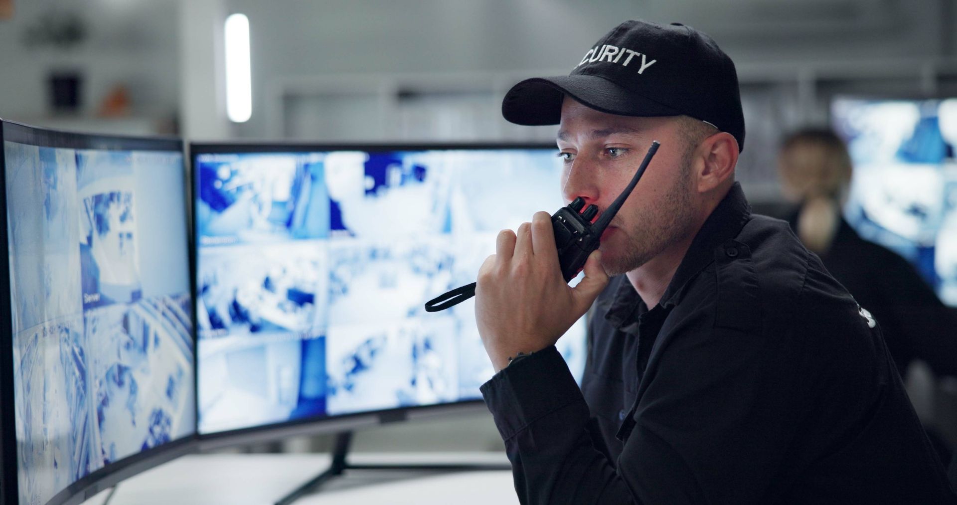 A security guard is talking on a walkie talkie while looking at a monitor.