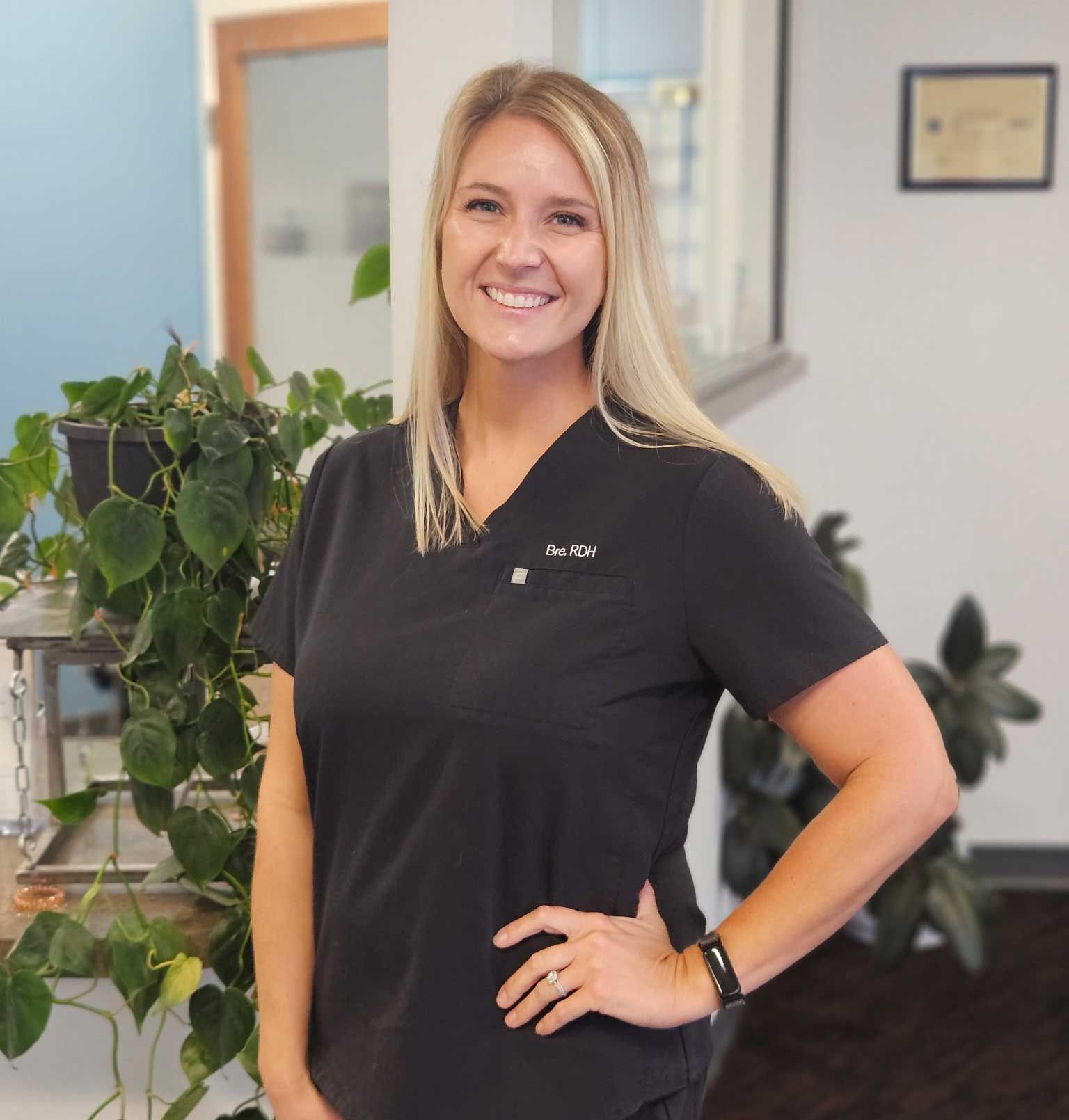 Smiling woman in black scrubs standing in a clinic hallway with plants in the background Smiling woman in black scrubs standing in a clinic hallway with plants in the background