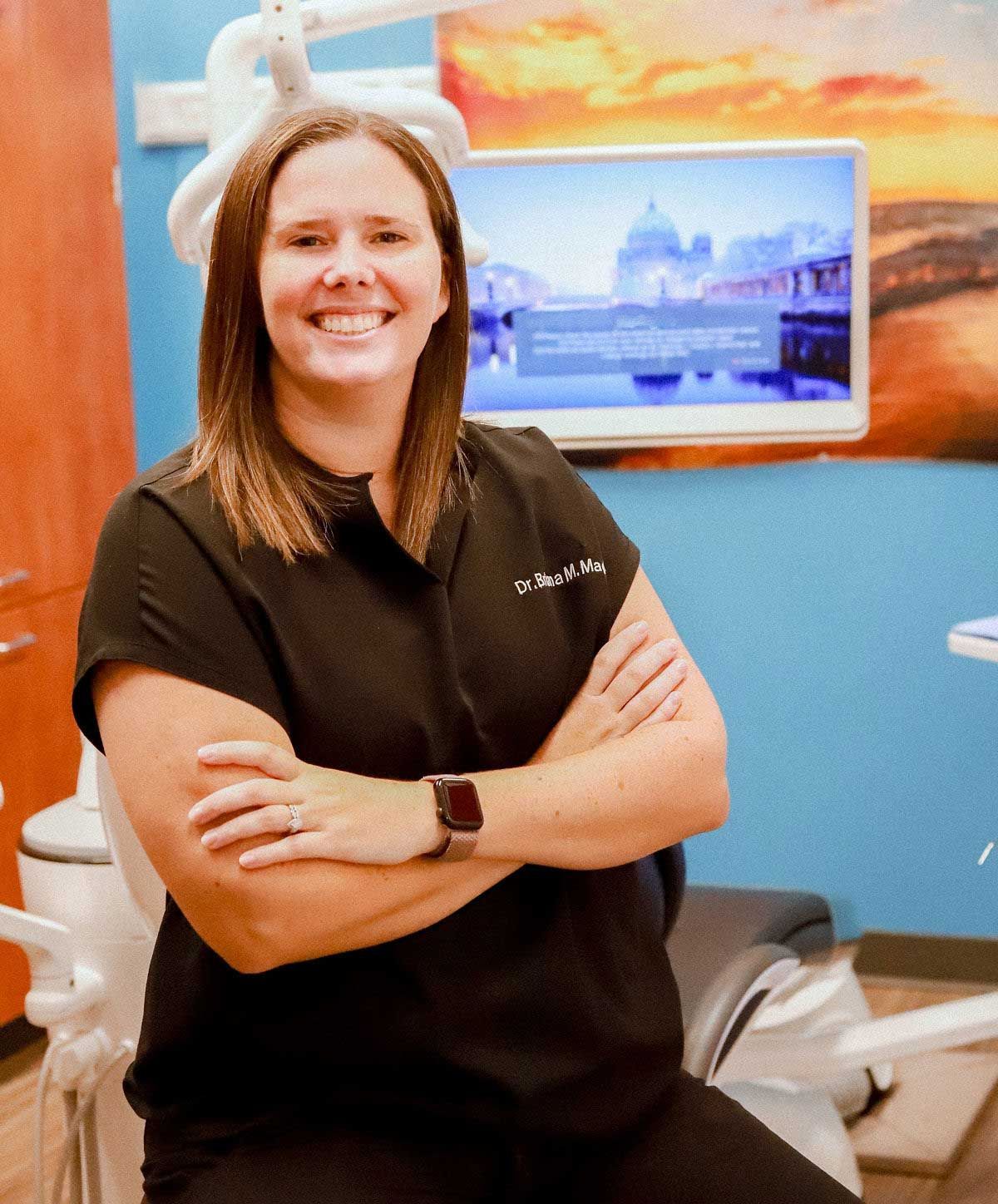 Smiling person in black scrubs with arms crossed, standing in a medical office. Smiling person in black scrubs with arms crossed, standing in a medical office.