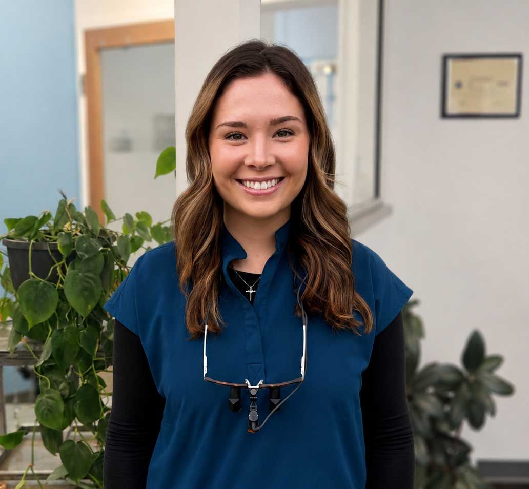 Woman smiling in a blue top, standing indoors with potted plants and office decor in the background Woman smiling in a blue top, standing indoors with potted plants and office decor in the background