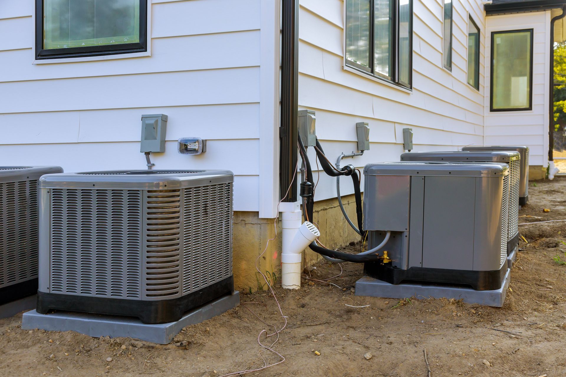 A row of air conditioners are sitting on the side of a house.
