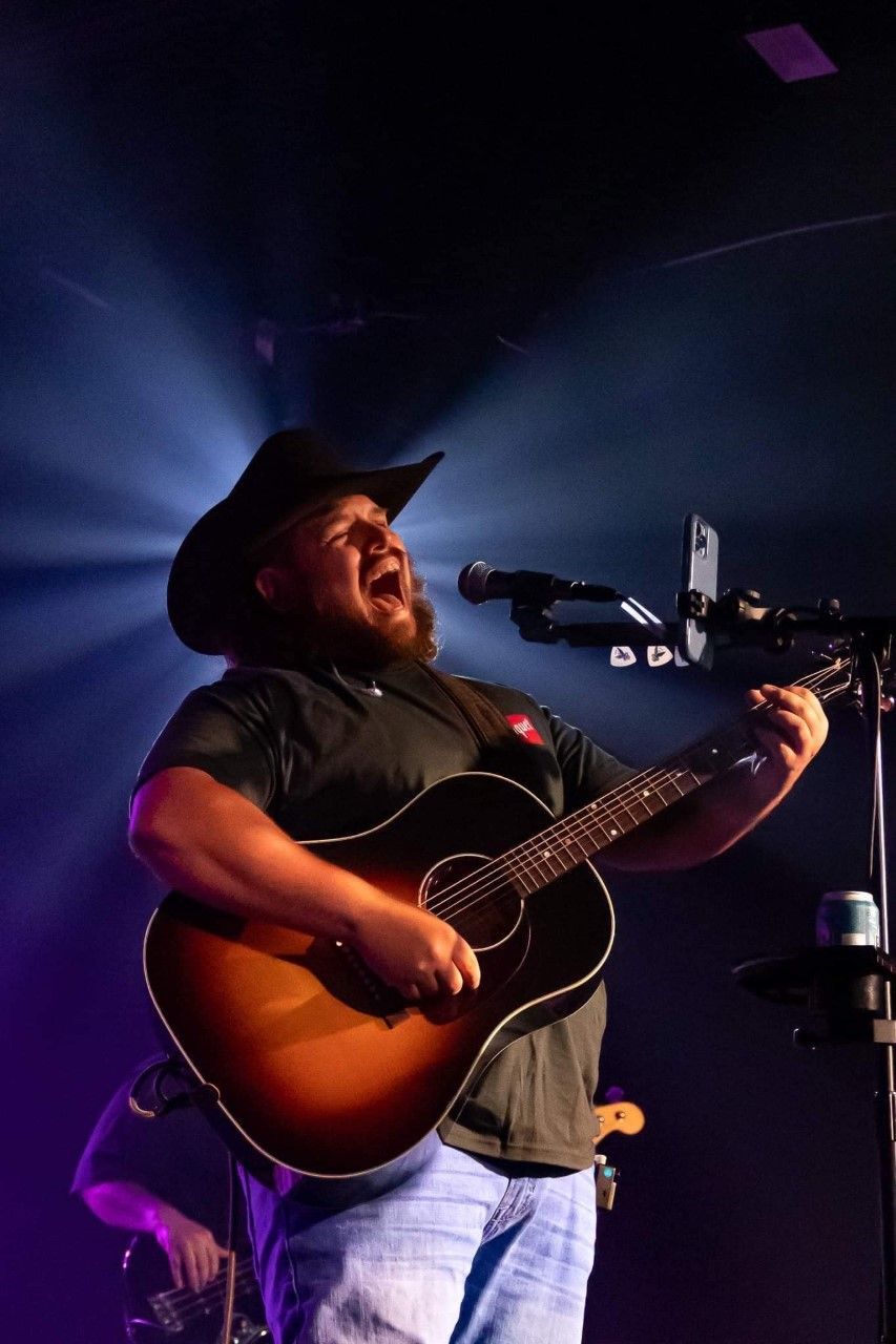 A man in a cowboy hat is singing into a microphone while holding a guitar.