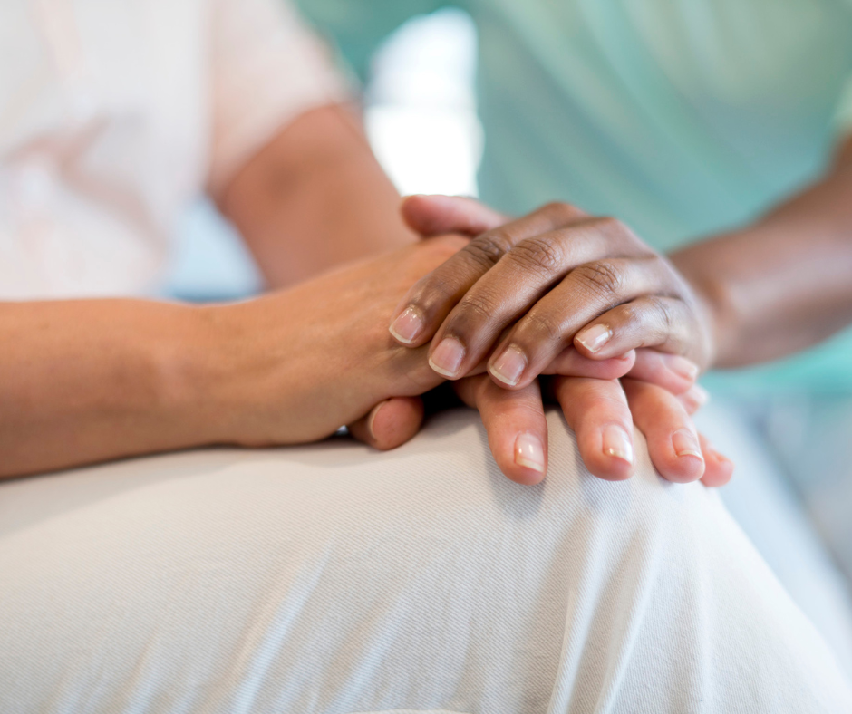 Two people’s hands resting together in a supportive gesture while seated.