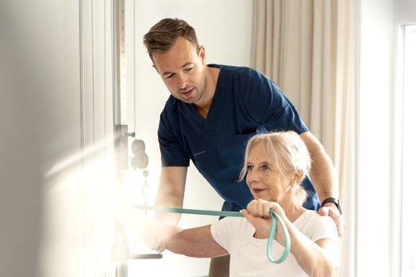 A healthcare professional assisting a patient with physical therapy exercises using a resistance band.
