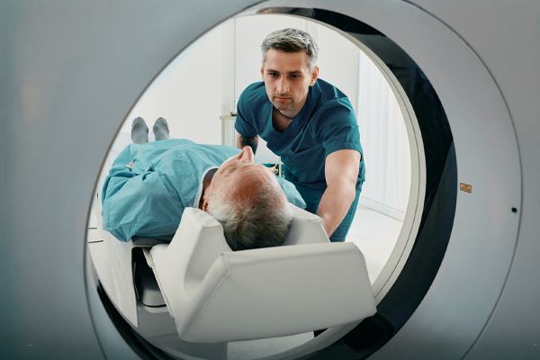 A medical technician prepares a patient lying on a motorized table for a scan inside a circular CT or MRI machine.
