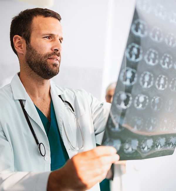 A doctor in a white coat and stethoscope examines a medical brain scan film.