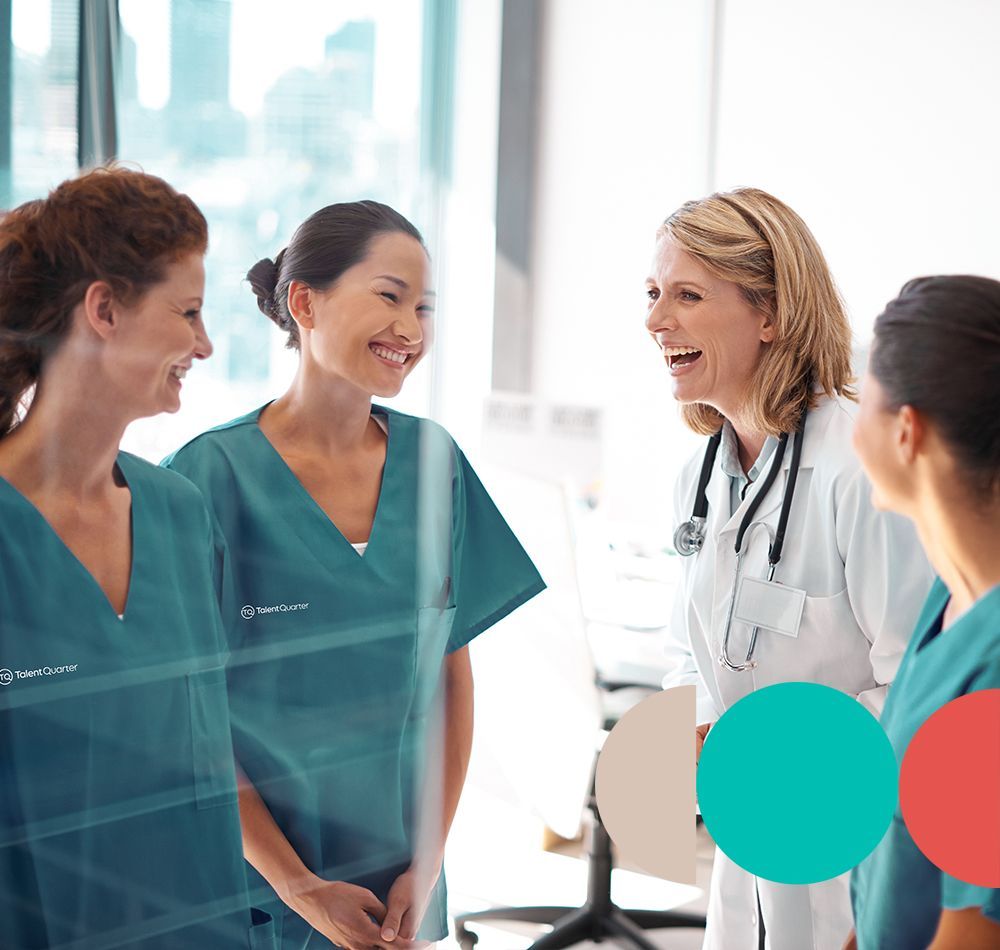 A diverse group of healthcare professionals in scrubs and a white coat laugh while standing together in an office setting.