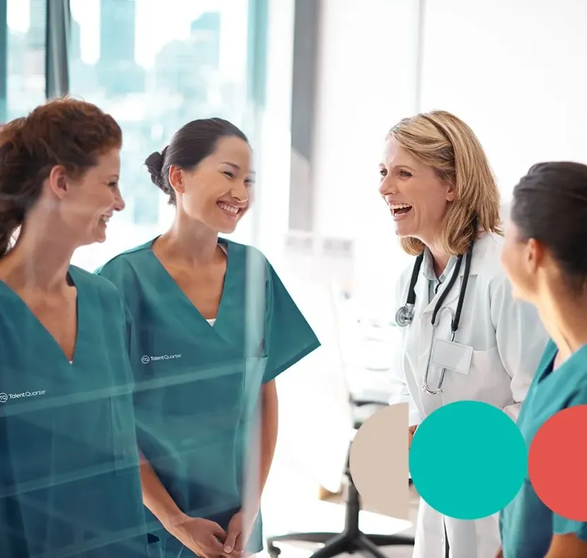 A group of medical professionals in scrubs and a lab coat talking and laughing in a bright, modern office space.