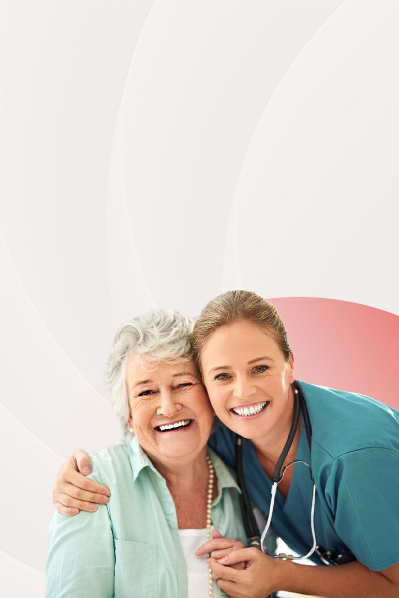 A caregiver in teal scrubs with a stethoscope smiles while arm-in-arm with a smiling individual in a light green shirt.