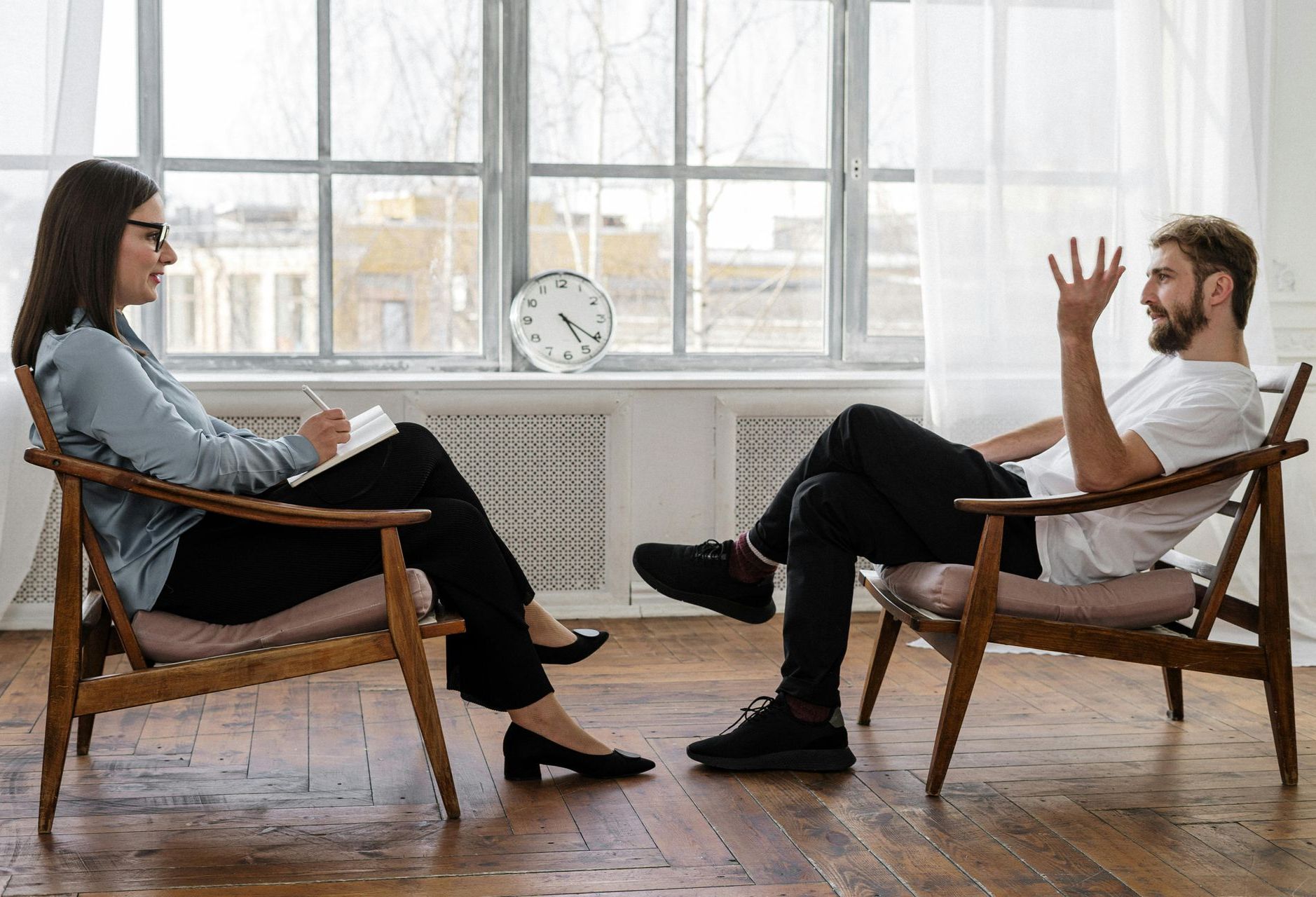 A person takes notes while sitting across from a person who is gesturing during a professional consultation.