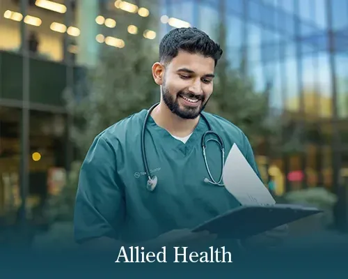 A person in green scrubs holds a folder and speaks on a mobile phone outside a glass building with the text 