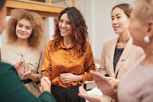 Four people in business attire smile and clap together in a professional setting.
