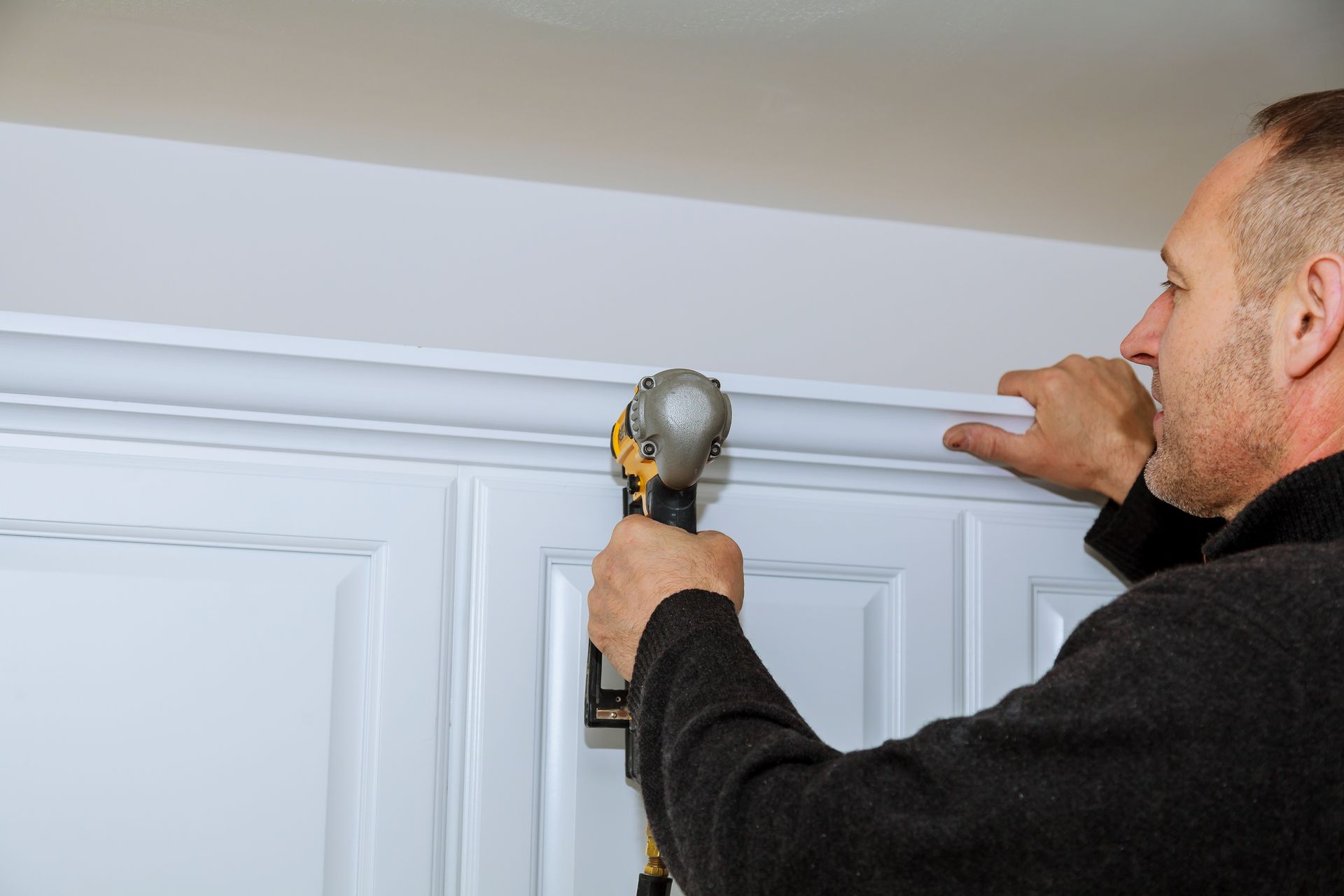 Un homme utilise une perceuse pour installer des moulures sur un mur.