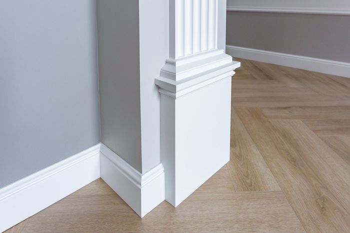Un coin d'une pièce avec moulures blanches et parquet.