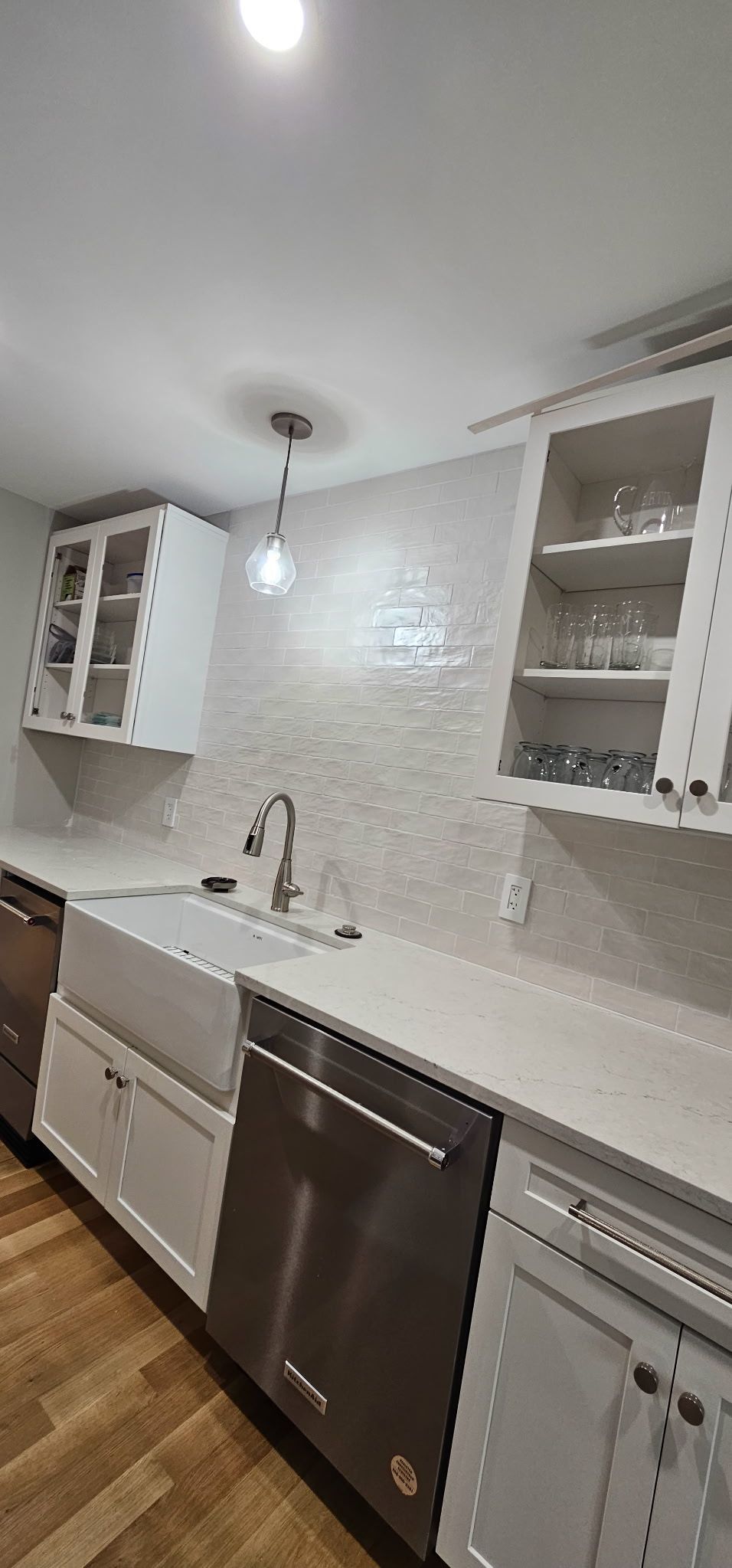 Modern white kitchen with mosaic tile backsplash, white cabinets, stainless steel dishwasher, and wood floor