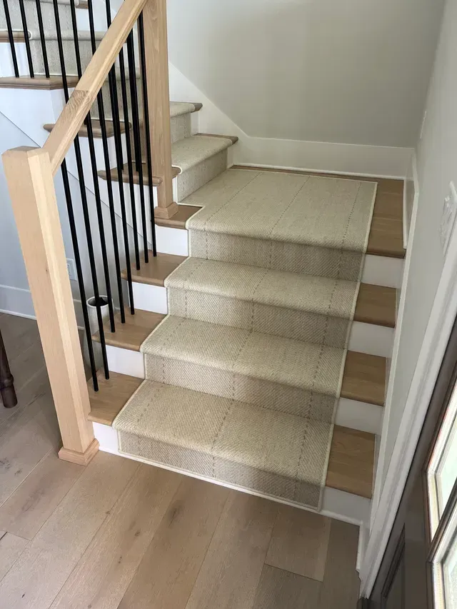 Carpeted staircase with wooden handrails and black balusters in a bright home interior