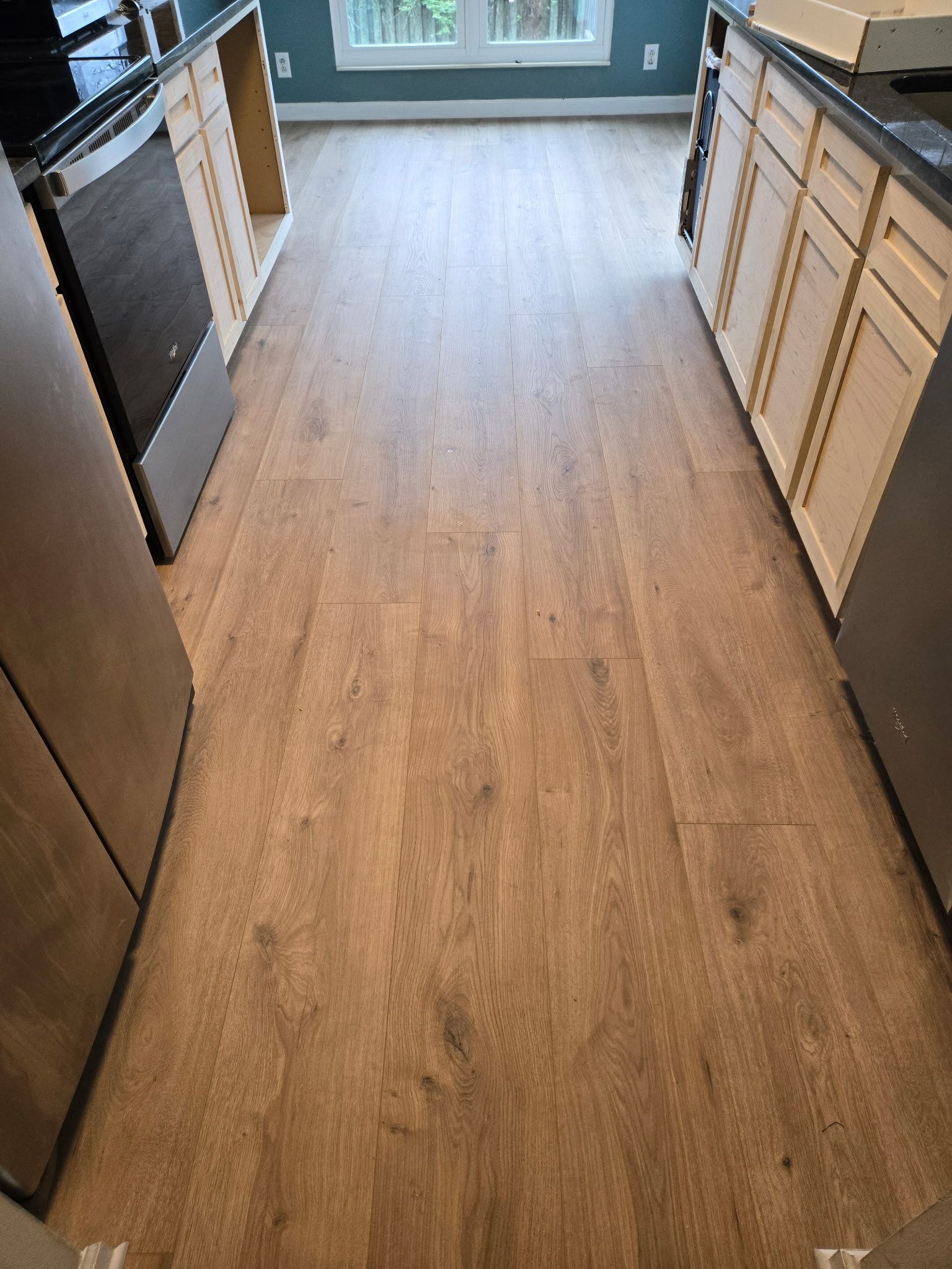 Narrow kitchen with wood-pattern flooring, light cabinets, and a window at the far end.