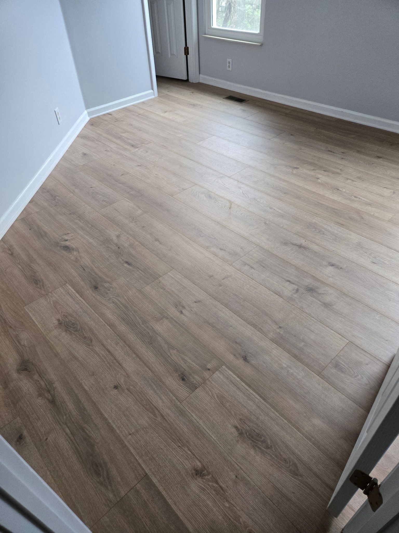 Empty room with light wood flooring, white walls, and a door near a window.
