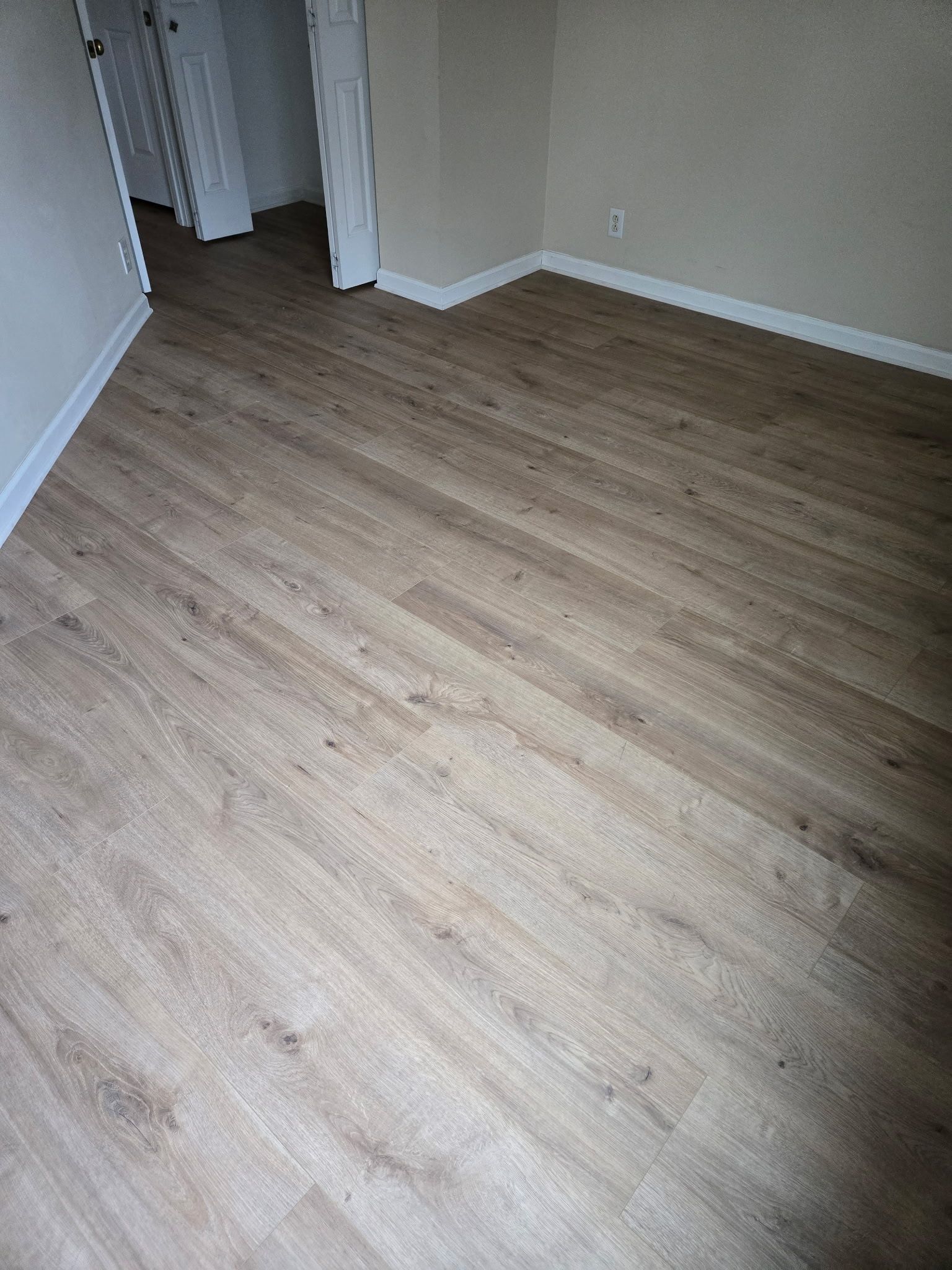 Empty room with light wood flooring, white walls, and a doorway in the corner