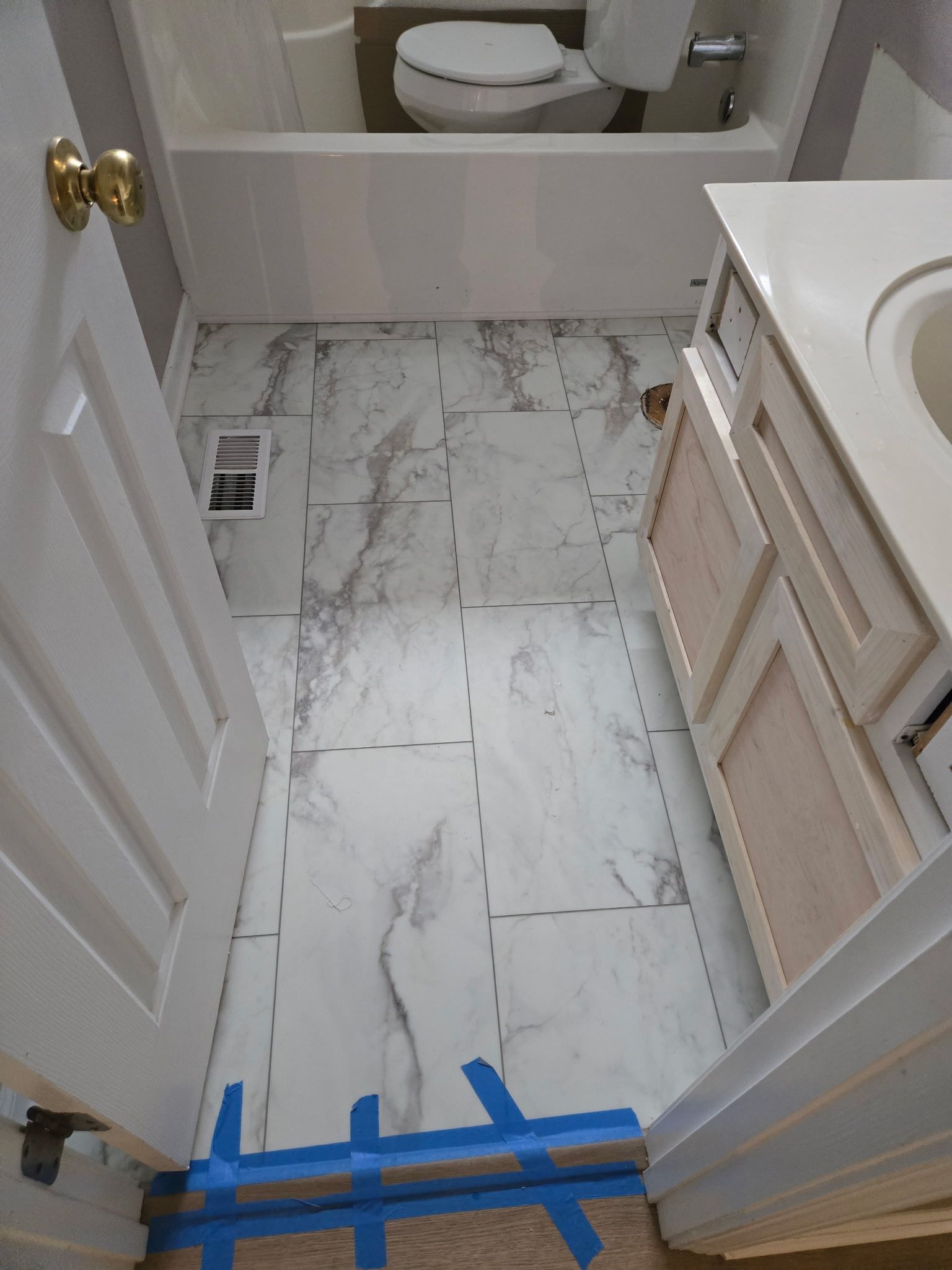 Bathroom hallway with marble-pattern flooring and blue tape marking a threshold near the toilet.