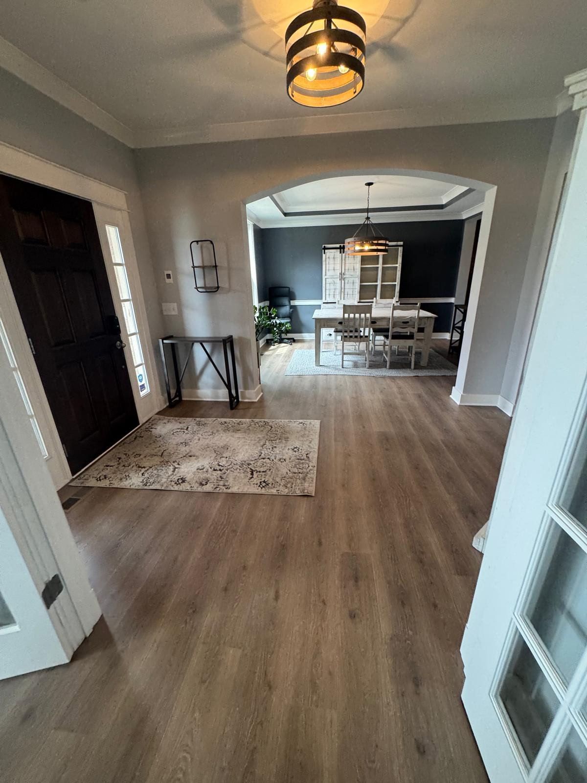 Bright hallway with wood floors, gray walls, and a view into a dining room through an archway.