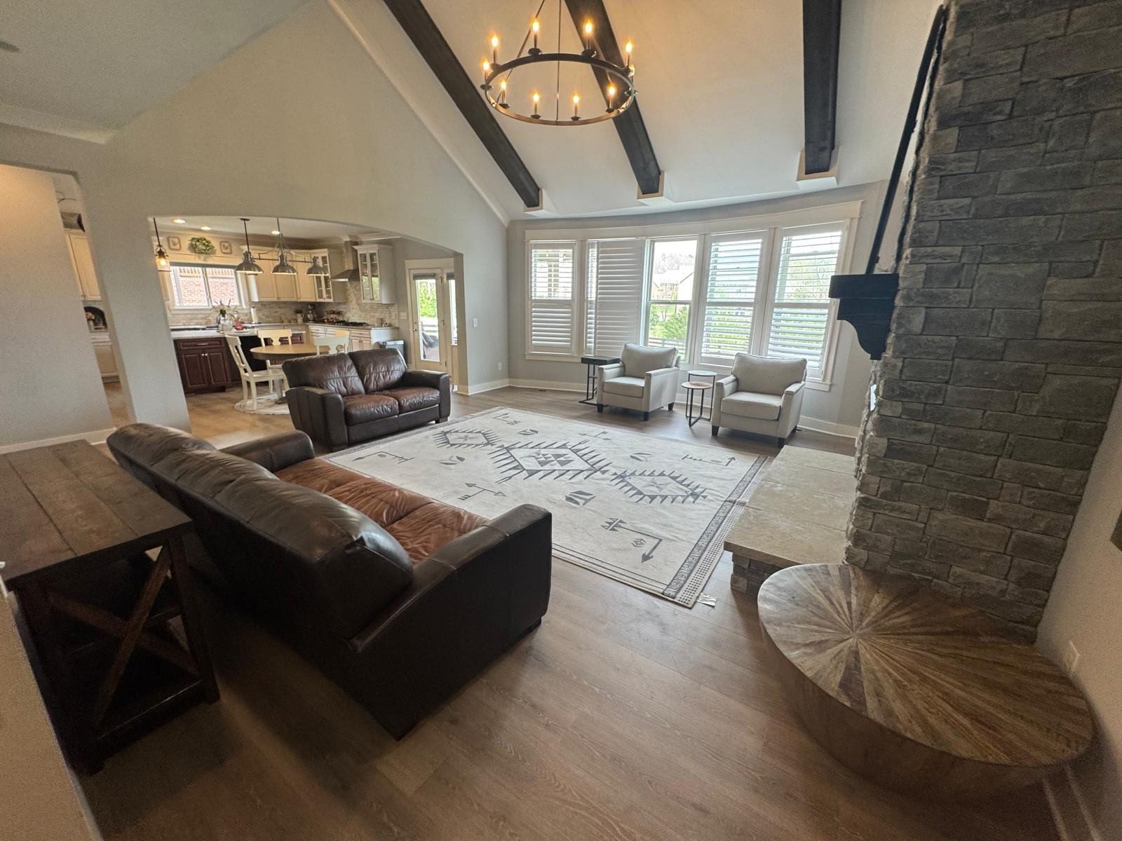Bright living room with stone fireplace, large windows, sectional sofa, and vaulted ceiling chandelier