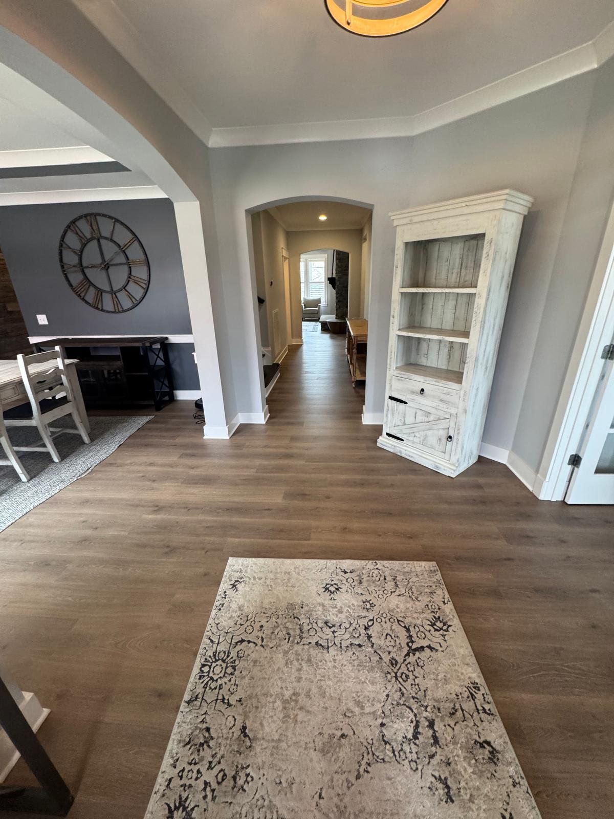 Bright living room with hardwood floors, gray walls, a patterned rug, and a white display cabinet.