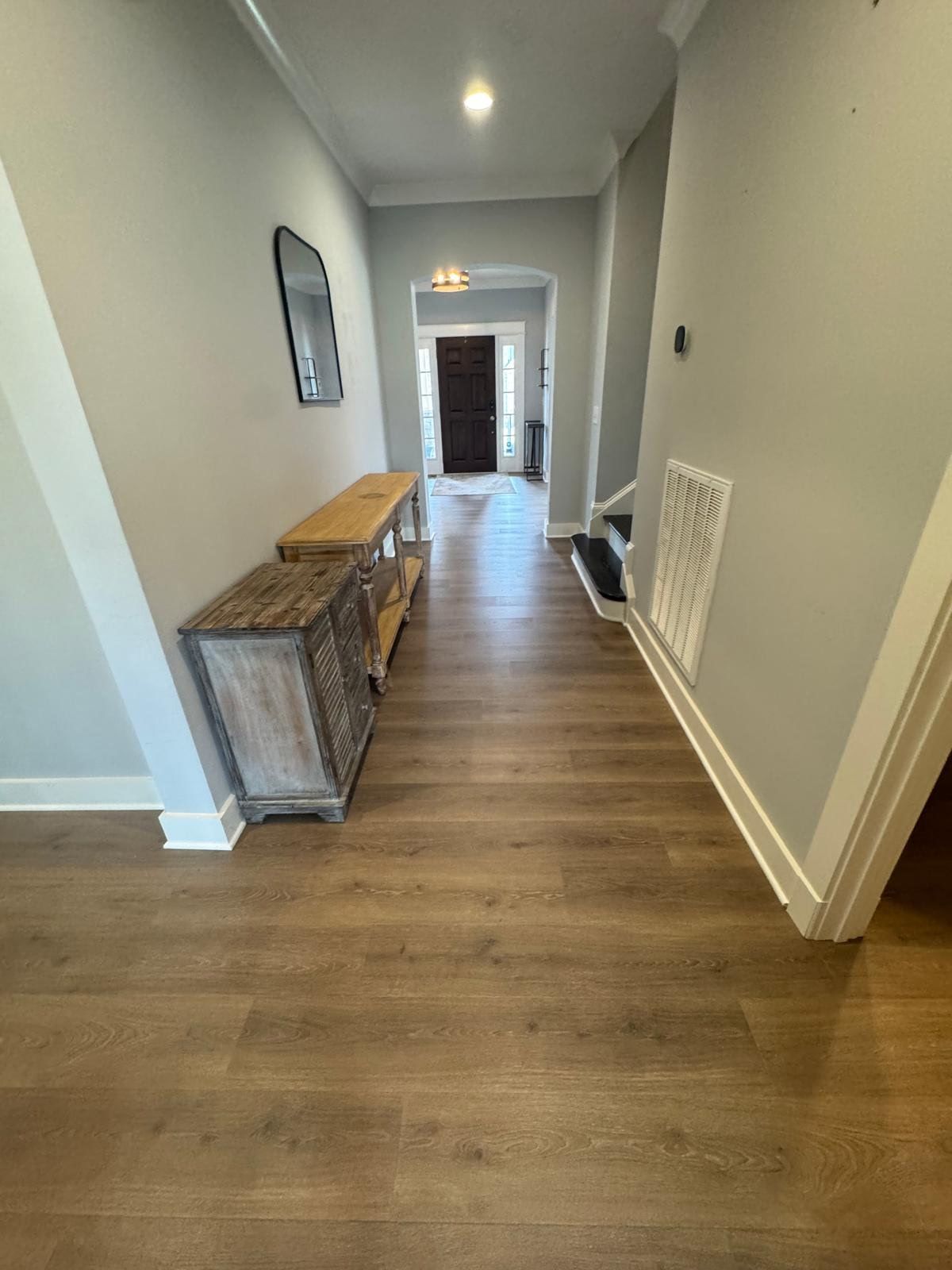 Long hallway with wood floors, white walls, console table, and front door at the end.