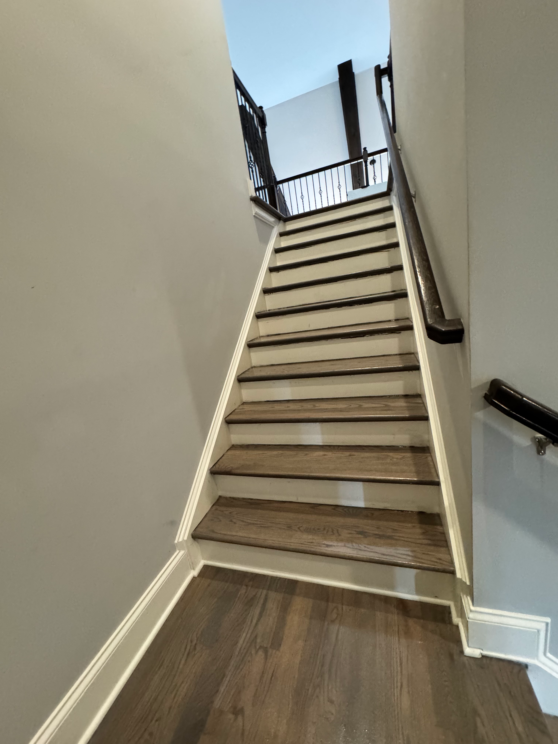 Narrow indoor staircase with carpeted steps and white walls, leading up to a landing with black railing