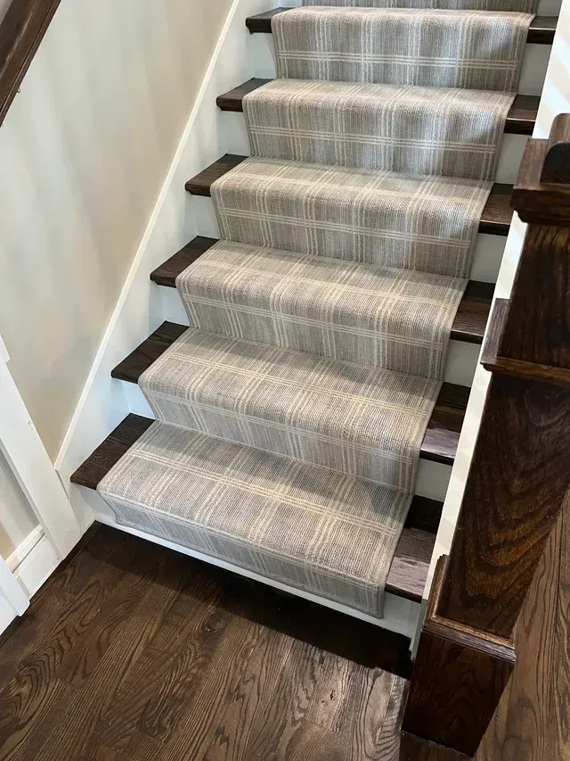 Carpeted staircase with gray runner and dark wood banister in a home interior
