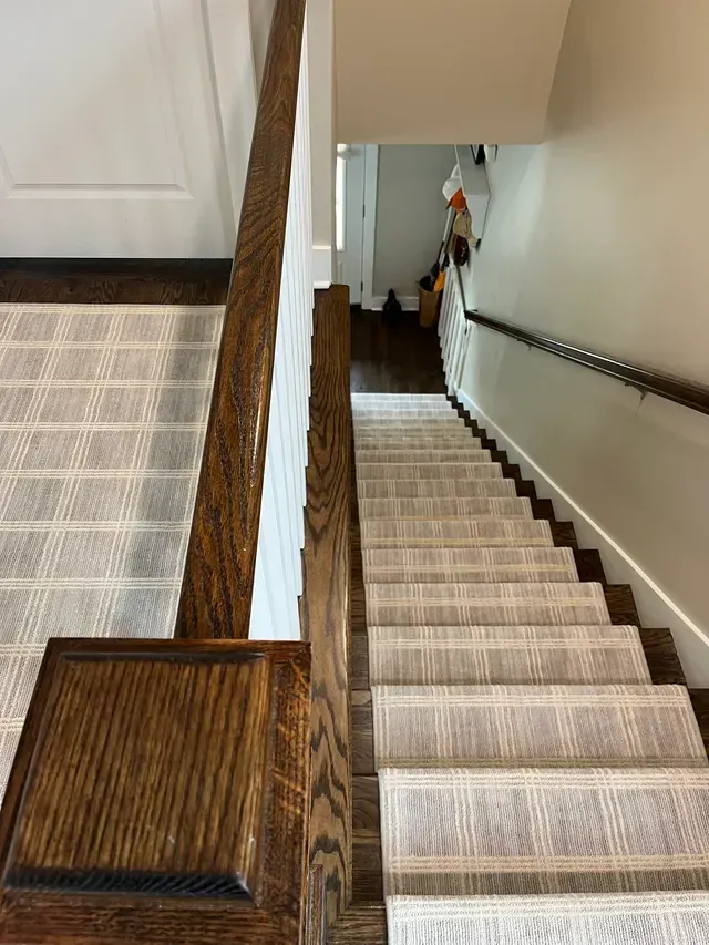 Staircase with beige carpet runner, wooden railing, and white walls in a home interior