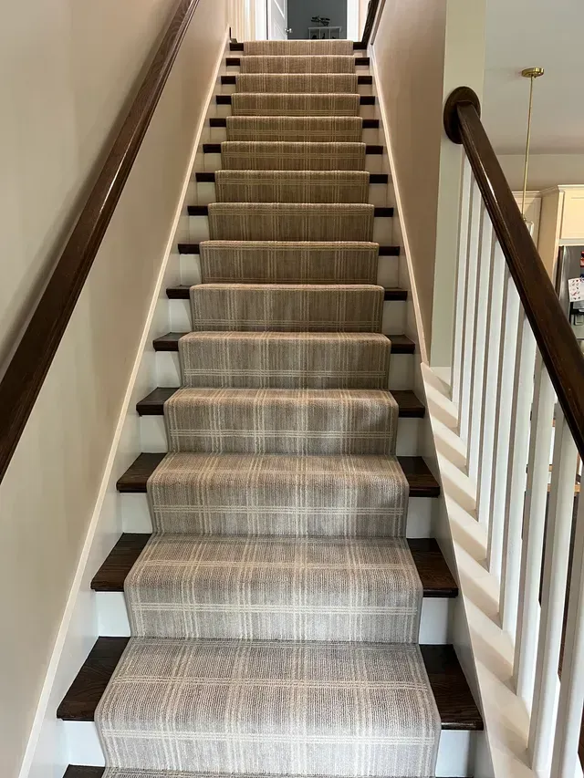 Carpeted staircase with white railings in a home interior, viewed from the bottom.
