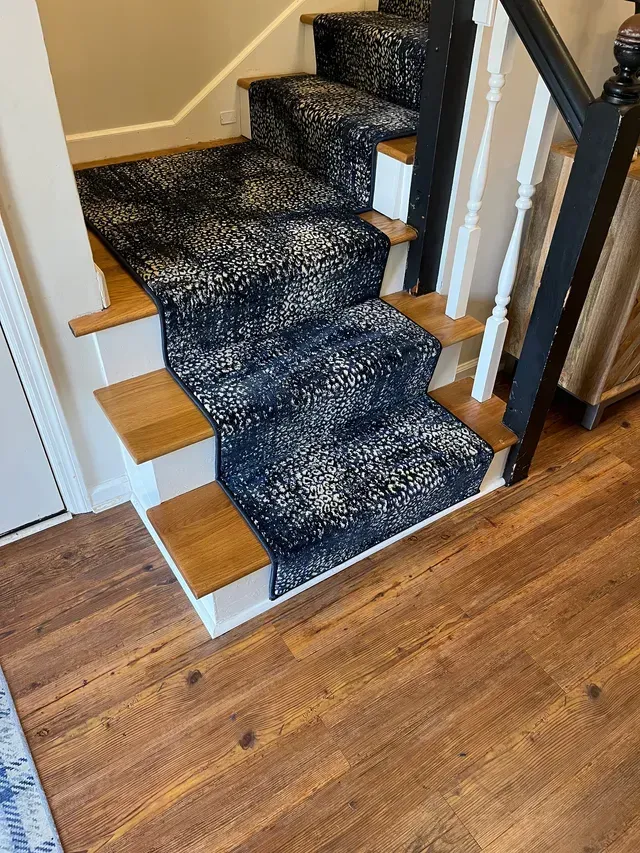 Carpeted staircase with dark patterned runner and wooden steps leading to a hardwood floor