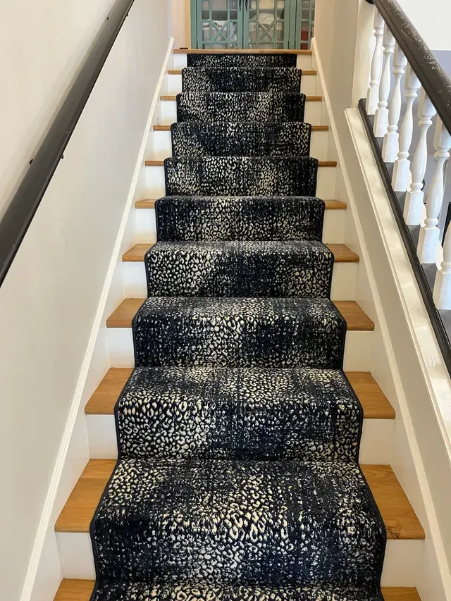 Narrow staircase with dark blue runner carpet and white railings on both sides.