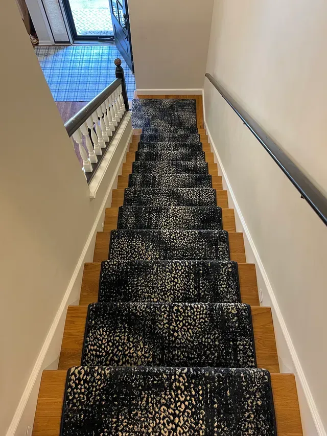 Narrow staircase with black carpet runner and white railings leading down to a hallway.