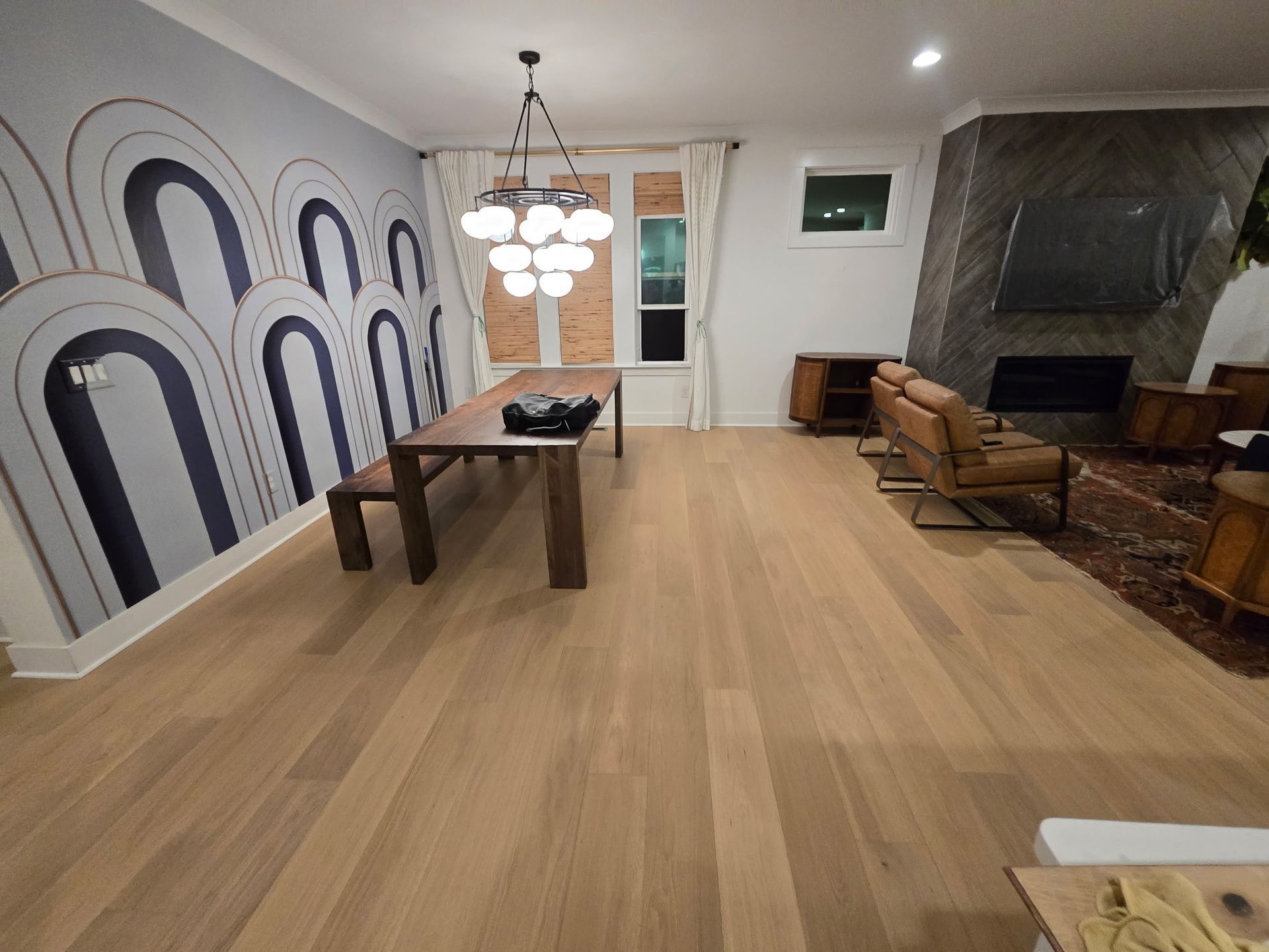 Modern living room with patterned accent wall, dining table, chandelier, and fireplace with seating area