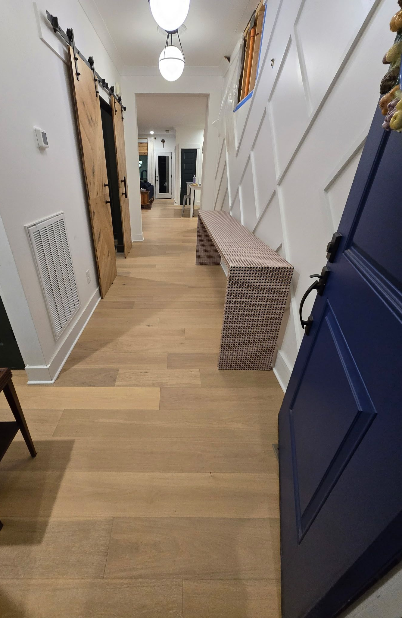 Narrow hallway with wood floors, white stairs, blue cabinets, and storage boxes along the walls