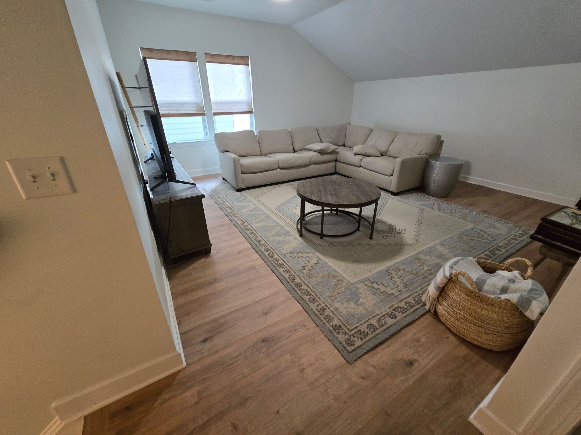 Bright living room with beige sectional, round coffee table, rug, and large window under sloped ceiling