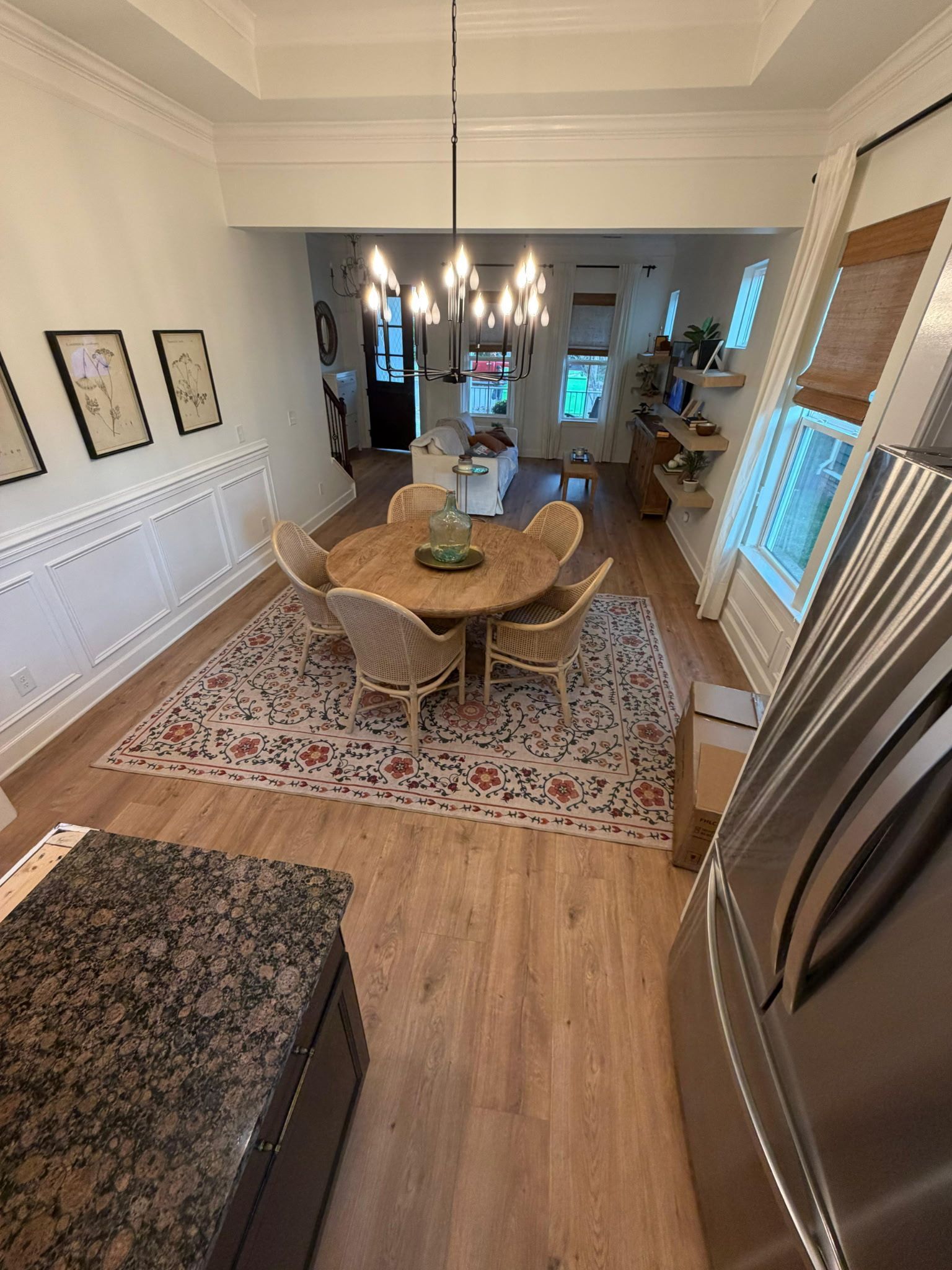 Dining room with wooden table, woven chairs, chandelier, patterned rug, and stainless steel refrigerator nearby