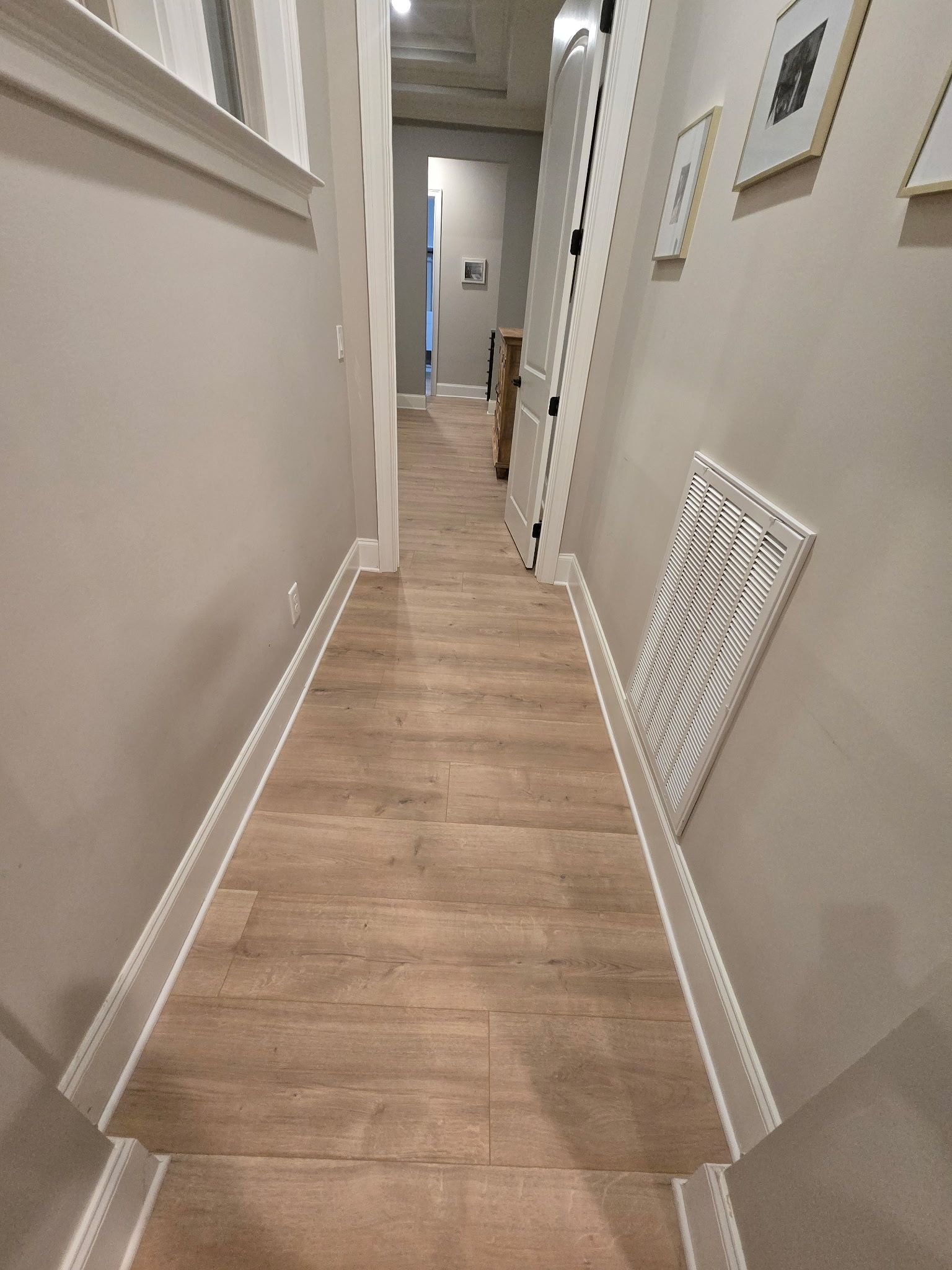 Narrow beige hallway with wood-look floor, wall art, and a towel hanging on the right wall.