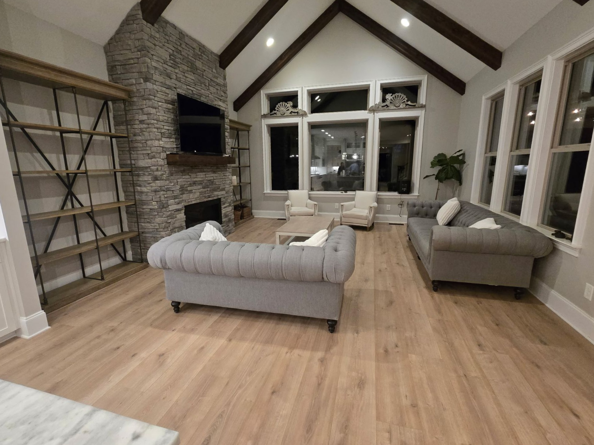 Spacious living room with vaulted ceiling, stone fireplace, gray sofa, and large windows.