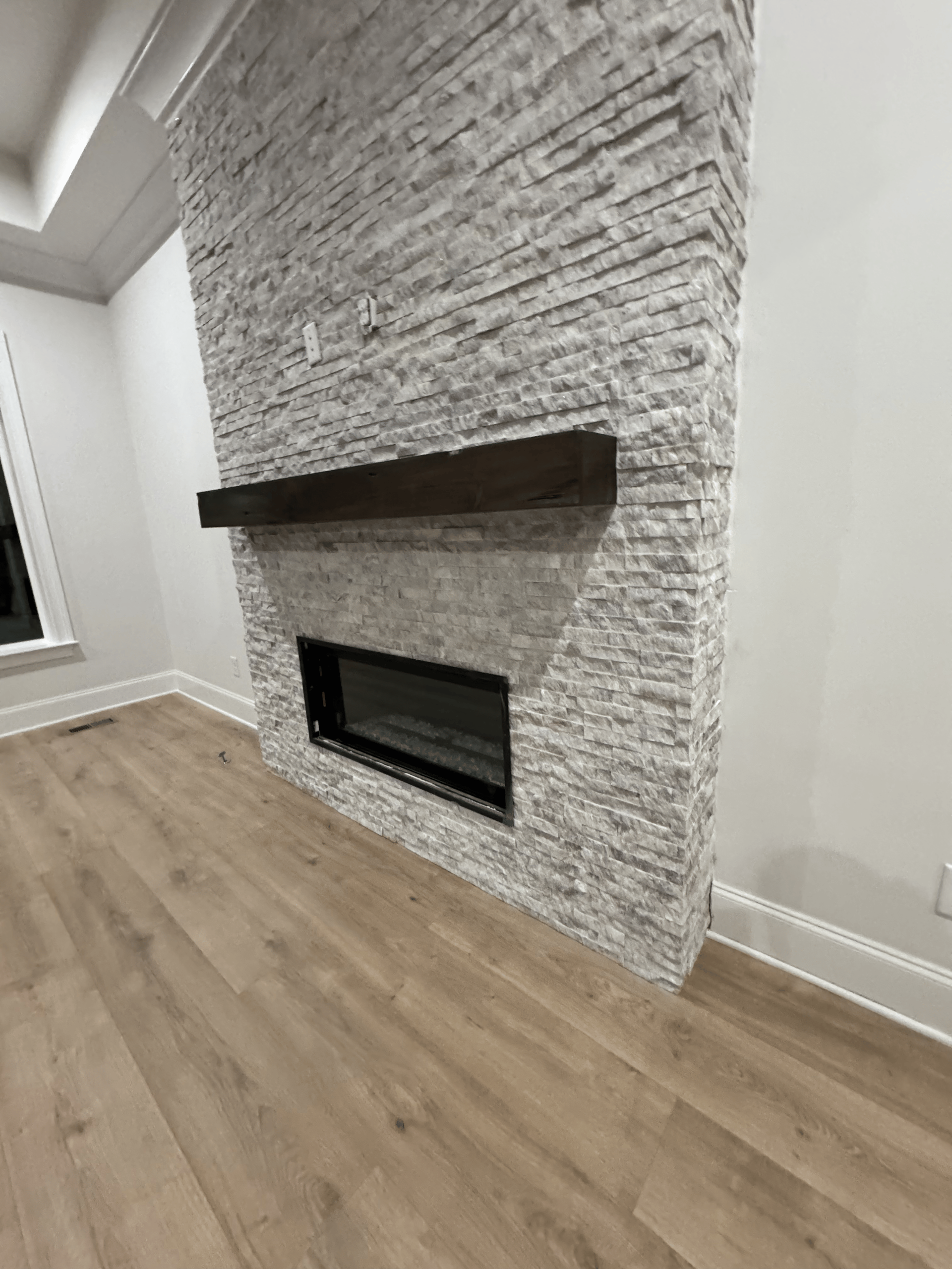 Modern room with white stone fireplace, dark mantel, and light wood flooring