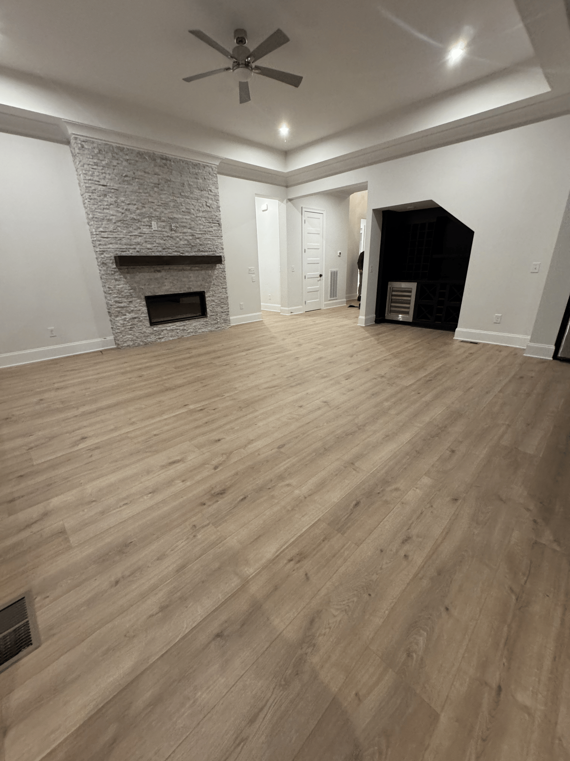 Spacious empty living room with wood floors, white walls, fireplace, and a dark built-in nook.