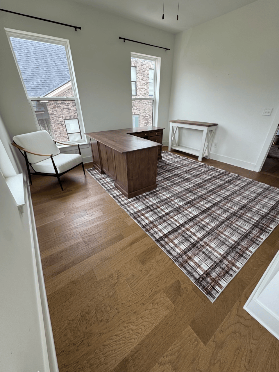 Bright room with chair, wooden desk, patterned rug, and two windows on hardwood floor.