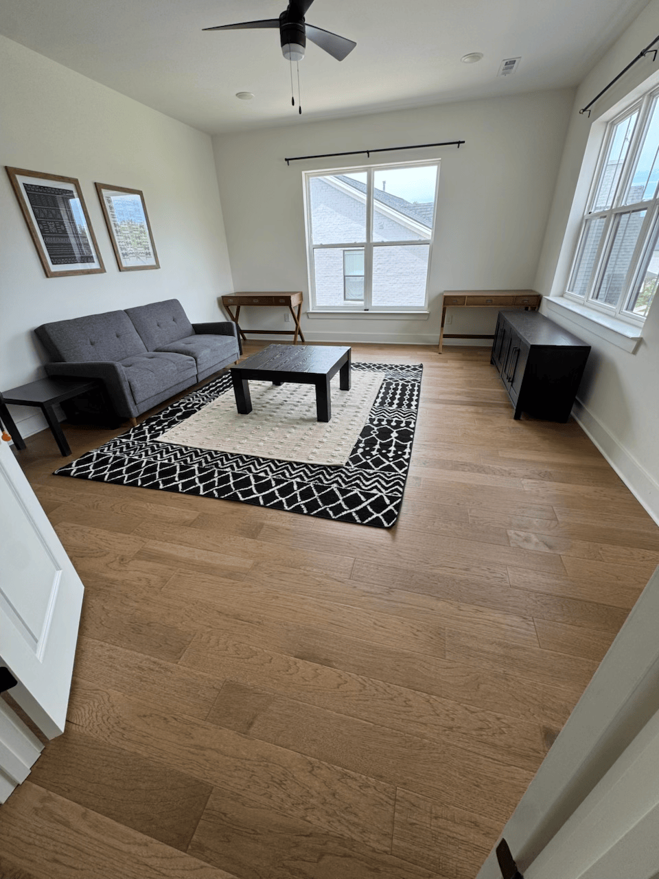 Empty living room with gray sofa, coffee table, patterned rug, and windows letting in natural light.