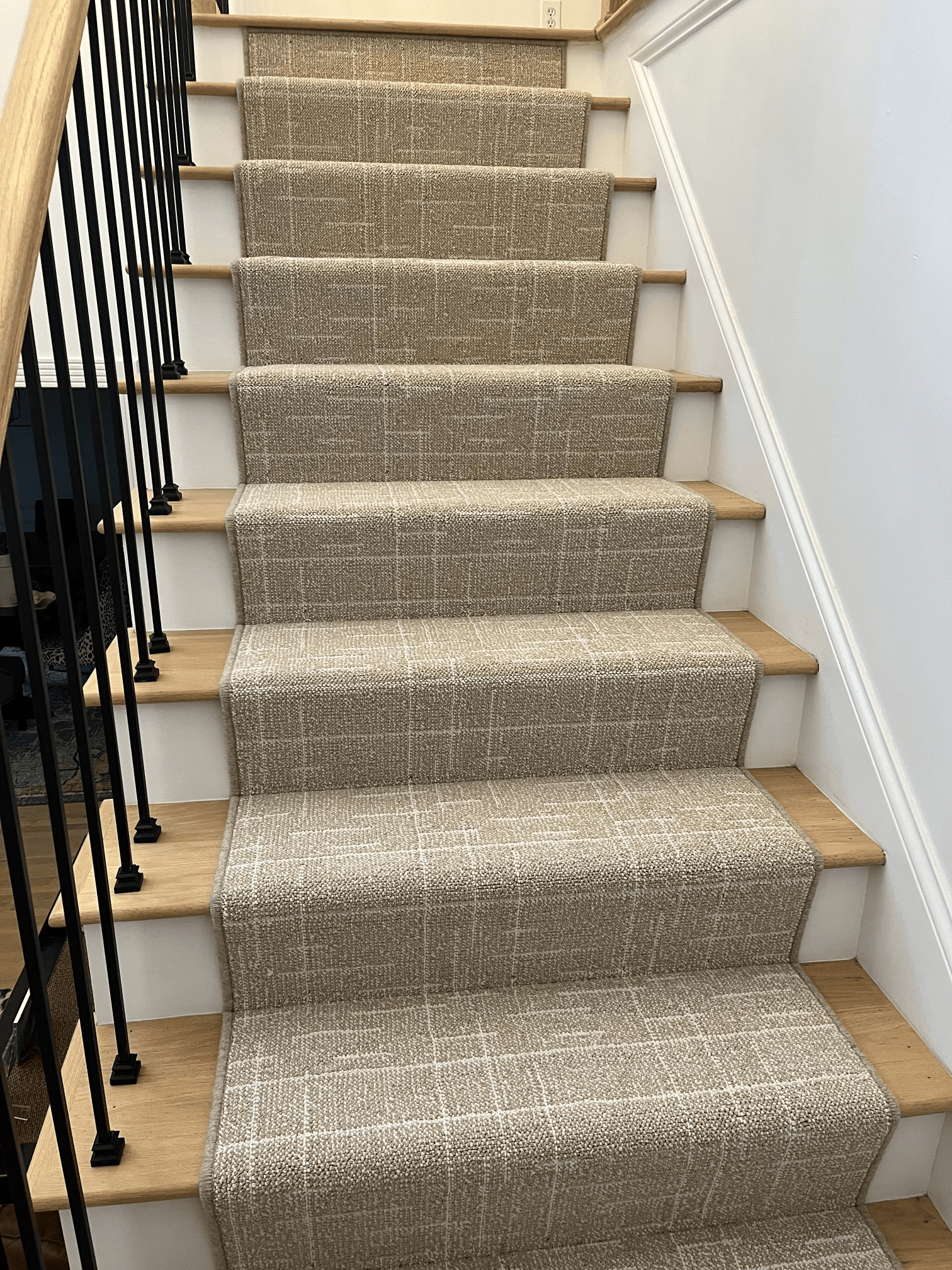 Carpeted staircase with beige steps and black railing in a narrow hallway