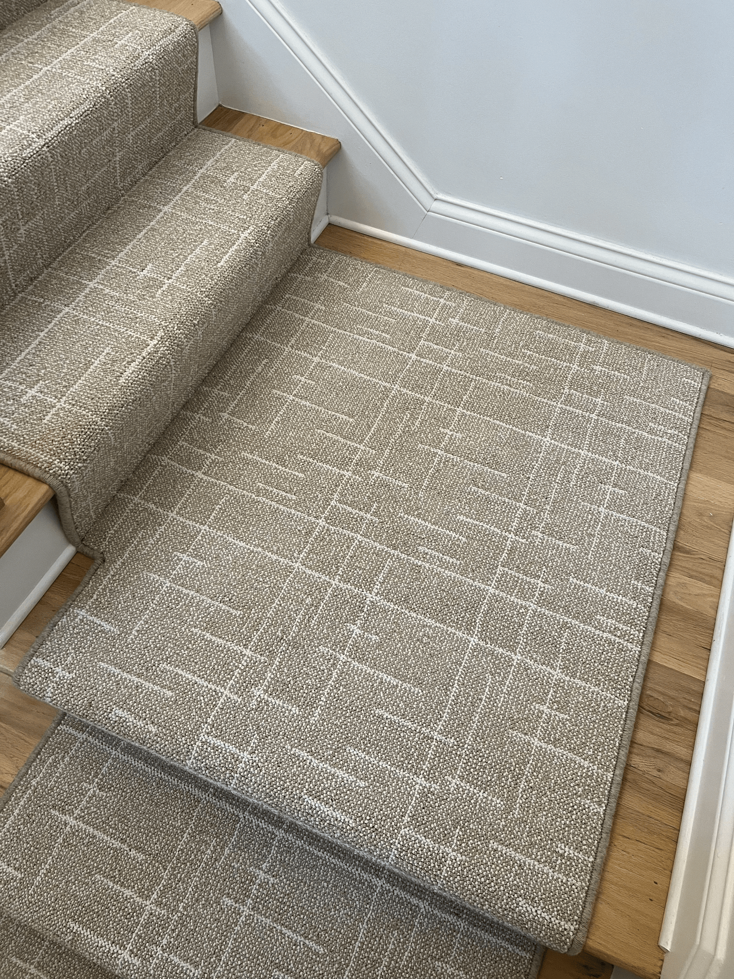 Carpeted stair landing with a beige rug over wood flooring beside gray stairs and white trim